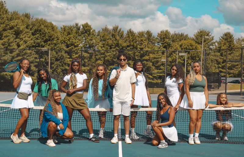 BSA members stand around a tennis net on a tennis court, all wearing tennis gear.
